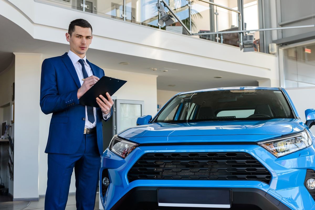 Young car dealer holding clipboard in salon